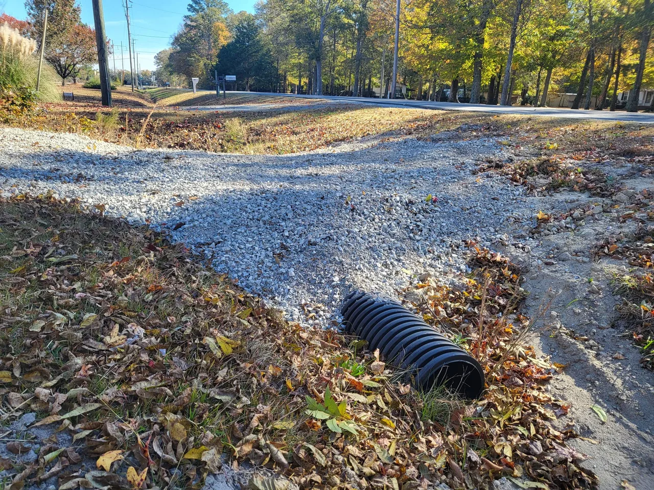 A black corrugated plastic culvert pipe under a new crushed stone driveway where it crosses a roadside ditch