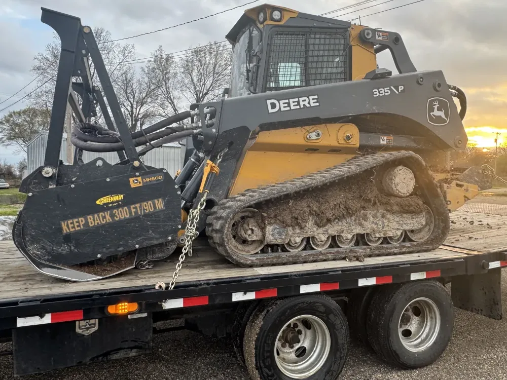 John Deere compact track loader with its forestry mulching head, chained down on the trailer